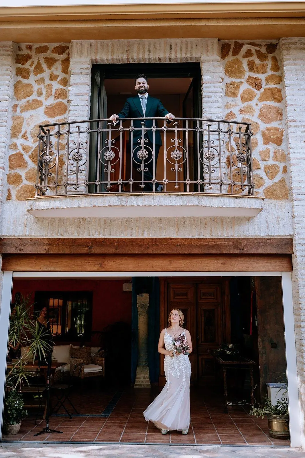 La novia en la puerta de la casa y el novio asomado al balcón