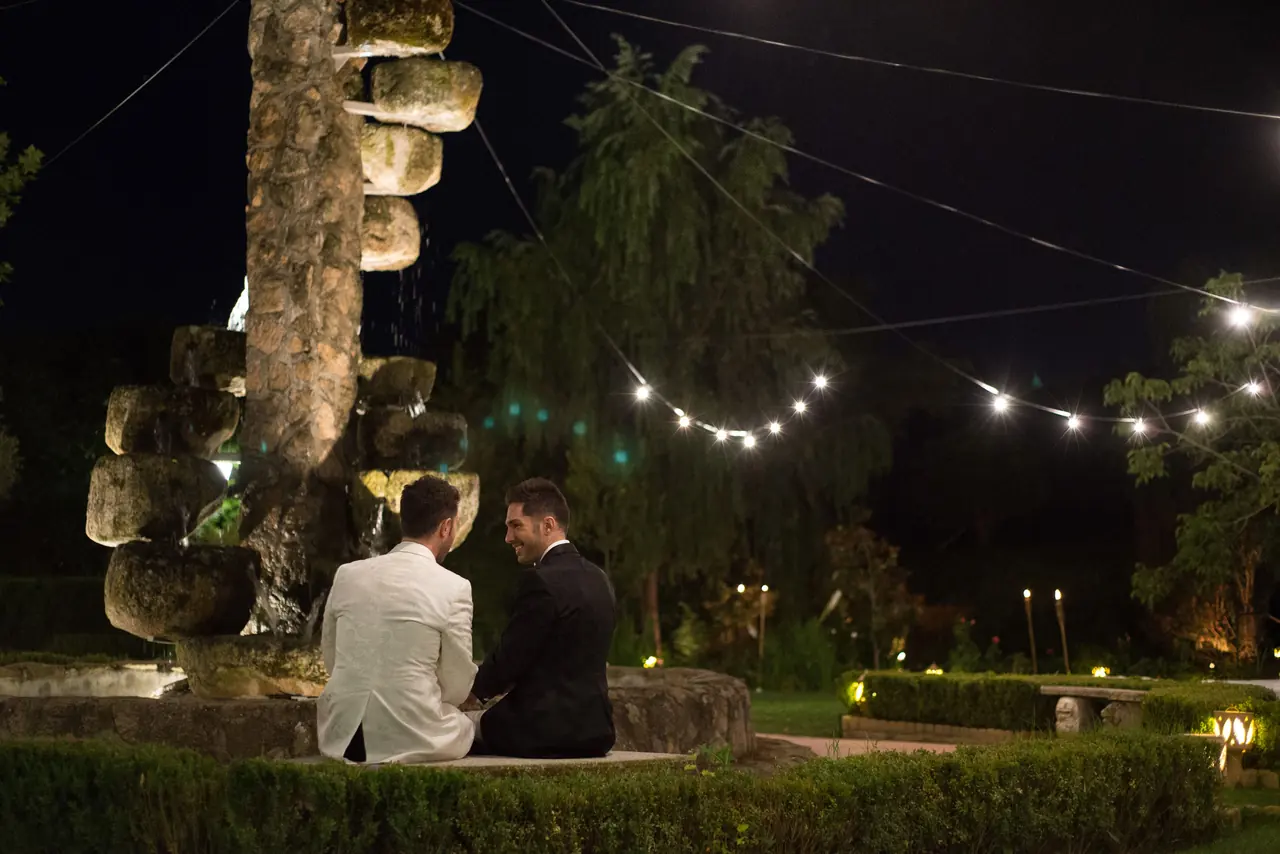 Los novios sentados junto a la fuente de noche, bajo guirnaldas de luces