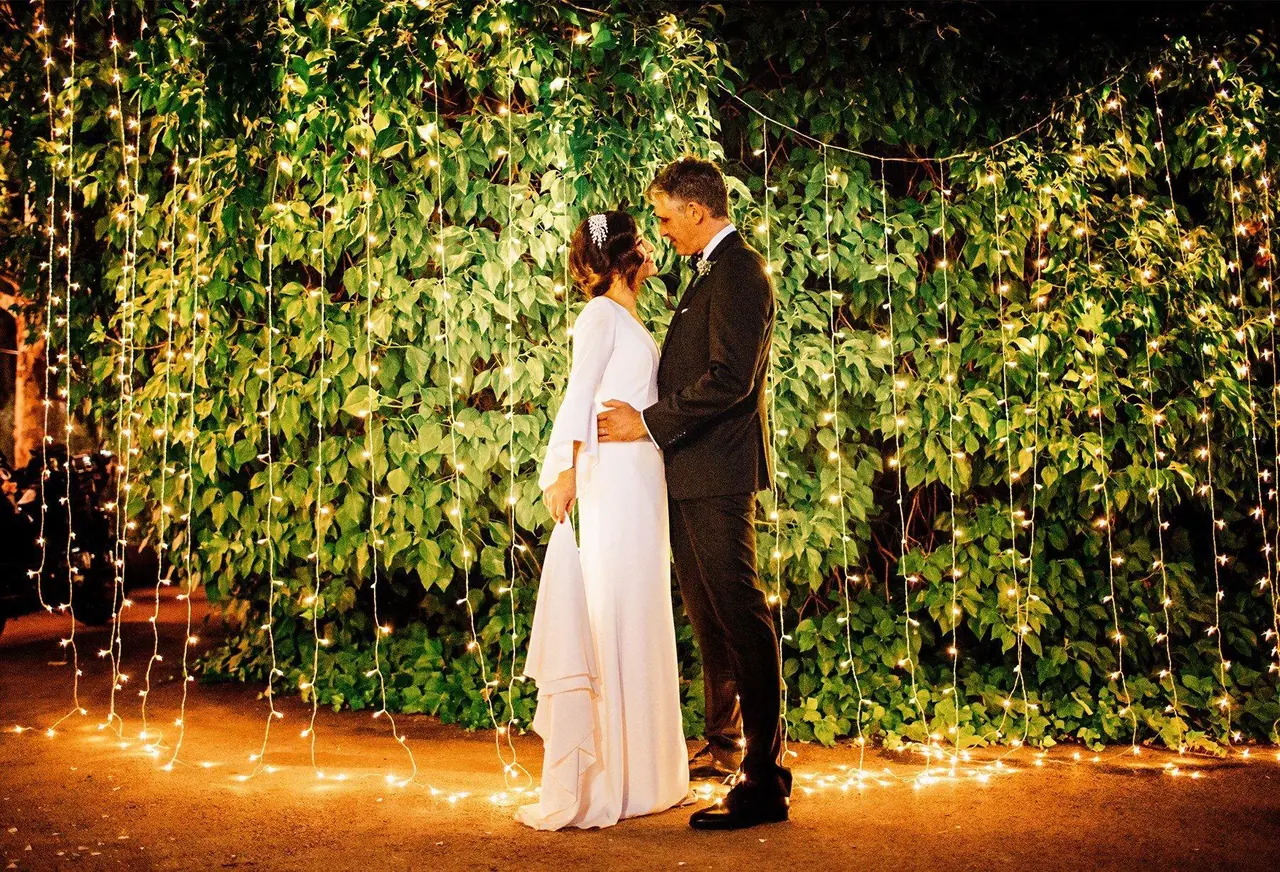 Novios bailando frente a una cortina de luces y hiedra