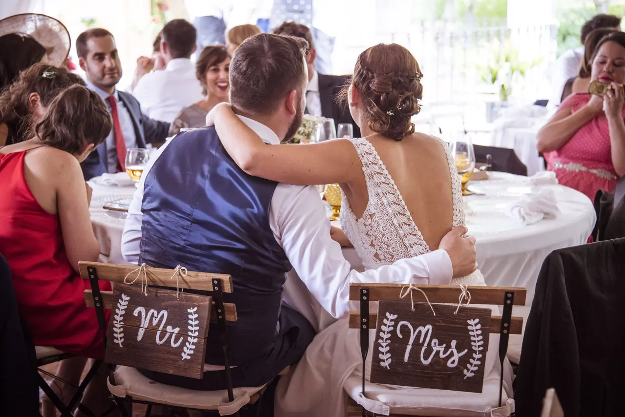Los novios en su mesa, en sillas con los carteles Mr y Mrs